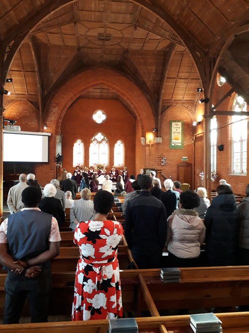 Congregation singing hymns during a Sunday service. Choir in the background, with the wooden ceiling of the church visible.